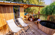Terraza soleada de madera en Océania Lodge, Domaine EcÔtelia, con tumbonas, bañera y zona de asientos.