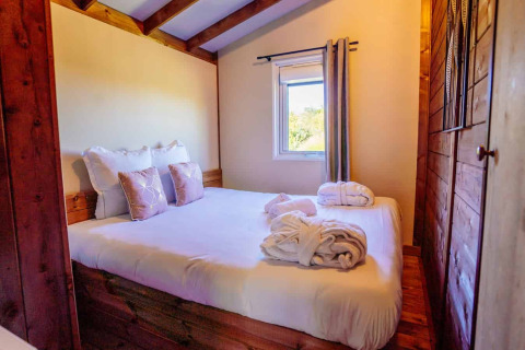 Gemütliches Schlafzimmer im Océania Lodge, Domaine EcÔtelia, Frankreich, mit Doppelbett und Bademänteln.