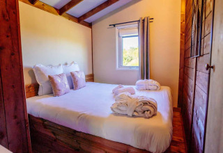 Gemütliches Schlafzimmer im Océania Lodge, Domaine EcÔtelia, Frankreich, mit Doppelbett und Bademänteln.