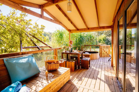 Sonnige Holzveranda mit Sitzbereich, Esstisch und Ausblick am Océania Lodge im Domaine EcÔtelia, Frankreich.