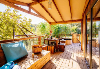 Sunny patio with wooden benches, dining table and green view at Océania Lodge, Domaine EcÔtelia, France.