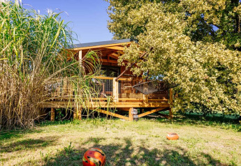 The Océania Lodge at Domaine EcÔtelia, France, a wooden cabin surrounded by greenery and trees on a sunny day.