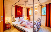Dormitorio en la cabaña 'Riad' de Domaine EcÔtelia, Francia, con cama con dosel, cortinas rojas y paredes de madera.