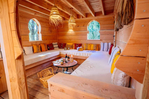 Gemütlicher Holzraum mit Sitzbereichen und bunten Kissen in der „Riad“-Lodge im Domaine EcÔtelia, Frankreich.