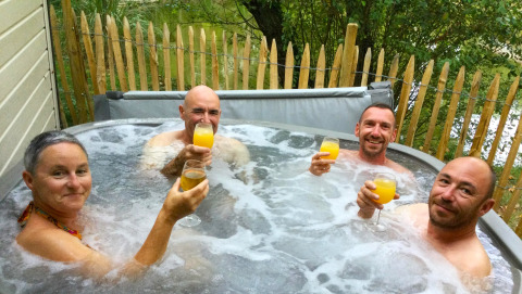 Quattro adulti si godono delle bevande nella vasca idromassaggio al Zen Mobile Home, Ushuaïa Villages Le Parc de la Grève, Francia.