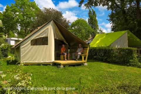 Deux personnes assises devant une tente Ecolodge au Ushuaïa Villages Le Parc de la Grève, France, entourées de verdure.