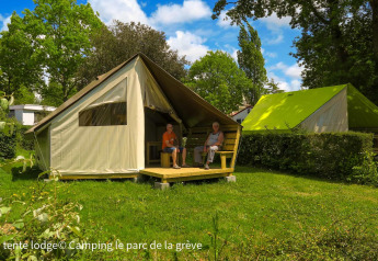 Deux personnes assises devant une tente Ecolodge au Ushuaïa Villages Le Parc de la Grève, France, entourées de verdure.