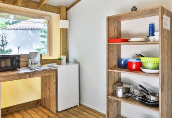Zona de cocina en la tienda safari Sahari Ecotent Mindervaliden, con estantería, microondas y nevera.