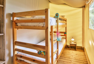 Lichte kamer in een safaritent met houten stapelbed, houten vloer en raam in Ushuaïa Villages Le Parc de la Grève.