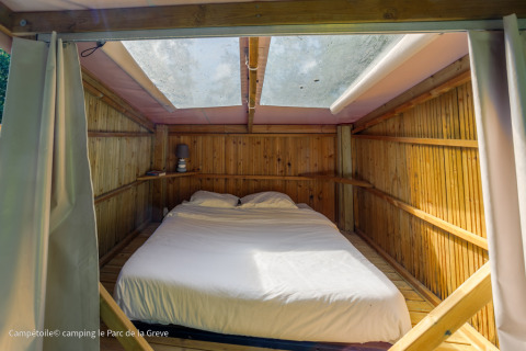 Vista interior de una tienda Campétoile con cama doble y tragaluz en Ushuaïa Villages Le Parc de la Grève, Francia.