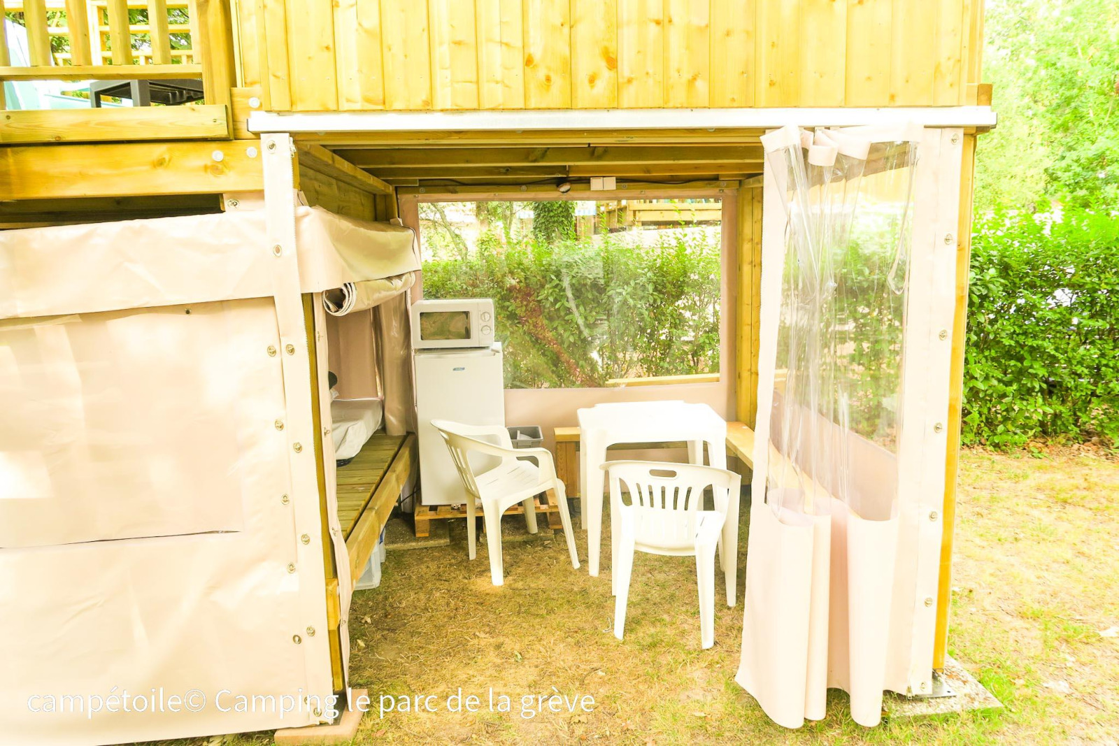 Buitenruimte onder een Campétoile tent met tafel, stoelen, koelkast en magnetron in Frankrijk.