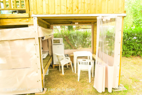 Zona exterior bajo una tienda Campétoile con mesa, sillas, frigorífico y microondas en Francia.