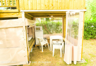 Zona exterior bajo una tienda Campétoile con mesa, sillas, frigorífico y microondas en Francia.
