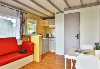 Interior del Relax Chalet con sofá rojo, cocina y mesa de comedor en Ushuaïa Villages Le Parc de la Grève, Francia.
