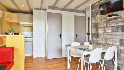 Interieur van Relax Chalet met eettafel, vier witte stoelen, wand-tv en keuken bij Ushuaïa Villages Le Parc de la Grève.