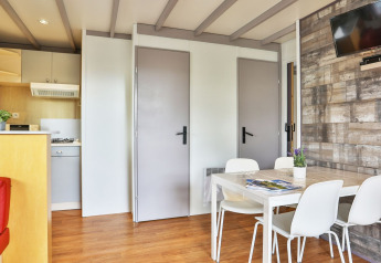 Interior del Relax Chalet con mesa de comedor, cuatro sillas blancas, televisor en la pared y cocina en Ushuaïa Villages Le Parc de la Grève.