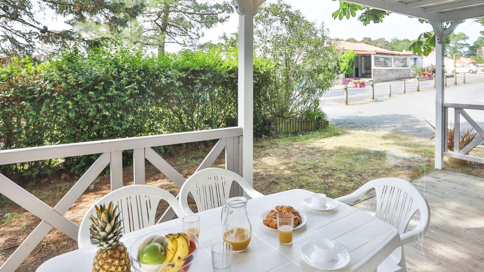 Buitenterras bij Relax Chalet met witte tafel, stoelen, fruit en sap, omringd door groen in Frankrijk