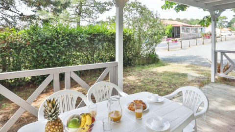 Buitenterras bij Relax Chalet met witte tafel, stoelen, fruit en sap, omringd door groen in Frankrijk