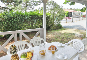 Terraza exterior en Relax Chalet con mesa y sillas blancas, fruta, zumo y vegetación en Francia