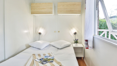 Lichte slaapkamer met tweepersoonsbed, nachtkastje en open raam in Relax Chalet van Ushuaïa Villages.