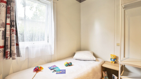 Heldere slaapkamer met eenpersoonsbed, speelgoed en raam in Relax Chalet Le Parc de la Grève, Frankrijk.