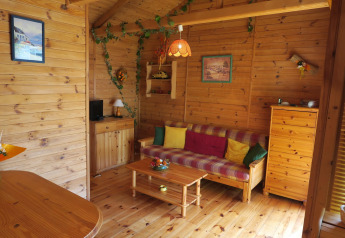 Indvendig udsigt til en hyggelig træhytte med farverige puder, trægulv og træmøbler i Ushuaïa Villages Le Parc de la Grève.