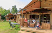 Family relaxing outside the Safari tent Vogelkers at Recreation park Kaps in the Netherlands with wooden furniture.