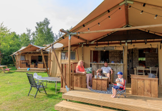 Family relaxing outside the Safari tent Vogelkers at Recreation park Kaps in the Netherlands with wooden furniture.