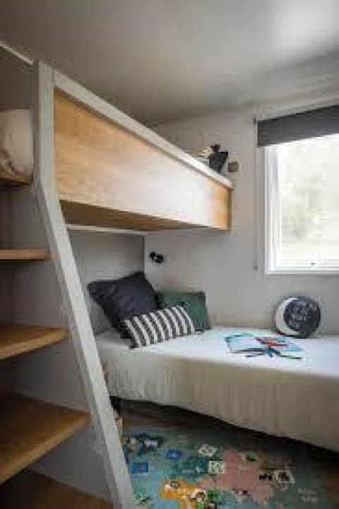 Chambre de mobil-home moderne avec lits superposés, tapis coloré et grande fenêtre à Flower Camping La Pointe du Talud.