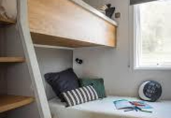Modern mobile home bedroom with bunk beds, colorful rug, and large window at Flower Camping La Pointe du Talud.