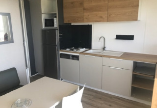 Modern kitchen with wood accents, table, and appliances inside Mobile home Premium LIVING in France.