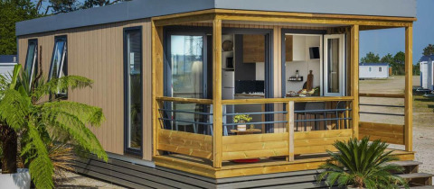 Contemporary Mobile home Premium LIVING with wooden porch, large windows, and lush plants in front.