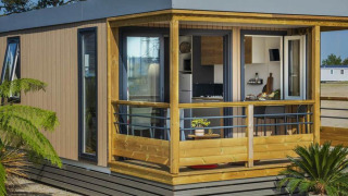 Contemporary Mobile home Premium LIVING with wooden porch, large windows, and lush plants in front.