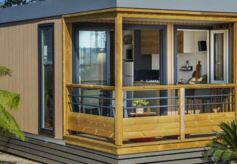 Casa móvil Premium LIVING moderna con porche de madera, grandes ventanales y plantas verdes al frente.