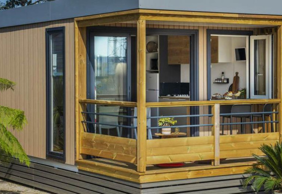 Casa mobile Premium LIVING moderna con veranda in legno, grandi finestre e piante verdi in primo piano.