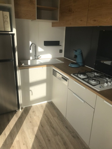 Modern kitchen with wood cabinets, gas stove, sink, and coffee maker in a mobile home at Camping La Pointe du Talud.