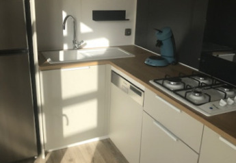 Modern kitchen with wood cabinets, gas stove, sink, and coffee maker in a mobile home at Camping La Pointe du Talud.