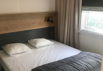 Schlafzimmer im Mobilheim „Premium EMBRUNS“ auf Flower Camping La Pointe du Talud, Bett mit Kissen und Decke.