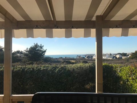 View from Mobile home Premium EMBRUNS terrace with awning, greenery, and the sea in the background.