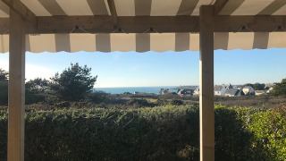 Vista desde la terraza de Mobile home Premium EMBRUNS con toldo, arbustos y el mar de fondo.