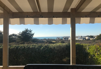 View from Mobile home Premium EMBRUNS terrace with awning, greenery, and the sea in the background.
