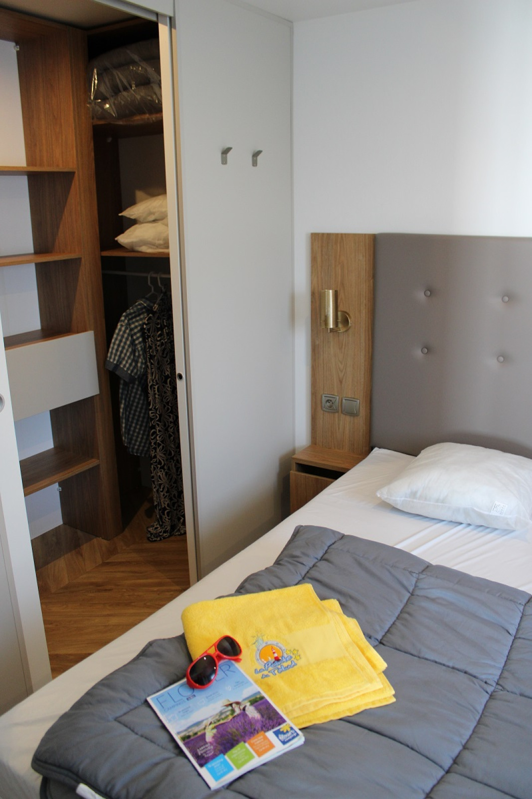 Slaapkamer van een stacaravan op Flower Camping La Pointe du Talud met bed, open kast en gele handdoeken.