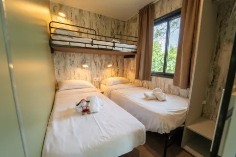 Habitación con dos camas individuales y una litera, gran ventana, en el Cottage Next XL Loggia de Trasimeno Glamping Resort, Italia.