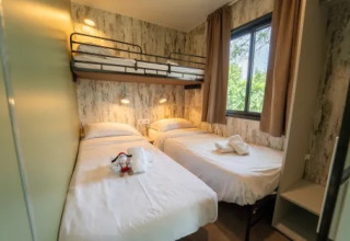 Habitación con dos camas individuales y una litera, gran ventana, en el Cottage Next XL Loggia de Trasimeno Glamping Resort, Italia.
