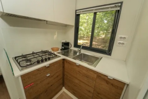 Cucinotto moderno con fornello a gas, lavello e finestra al Cottage Next XL Superior, Trasimeno Glamping Resort, Italia.