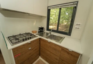 Cucinotto moderno con fornello a gas, lavello e finestra al Cottage Next XL Superior, Trasimeno Glamping Resort, Italia.