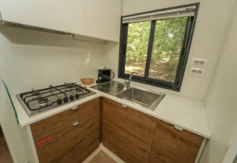 Cocina moderna con estufa de gas, fregadero y ventana en Cottage Next XL Superior, Trasimeno Glamping Resort, Italia.