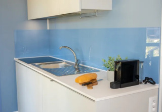 Cocina pequeña y moderna con fregadero, pan, cuchillo y cafetera en el Cottage Next XXL en Trasimeno Glamping Resort.
