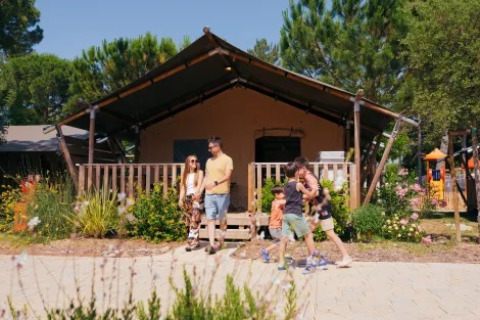 Family standing and walking in front of Safari Tent Comfort 'Trasimeno' at Trasimeno Glamping Resort, Italy.