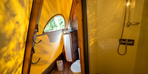 Badkamer in een Tipi Lodge tent met gele zeil en douche bij Trasimeno Glamping Resort, Italië.